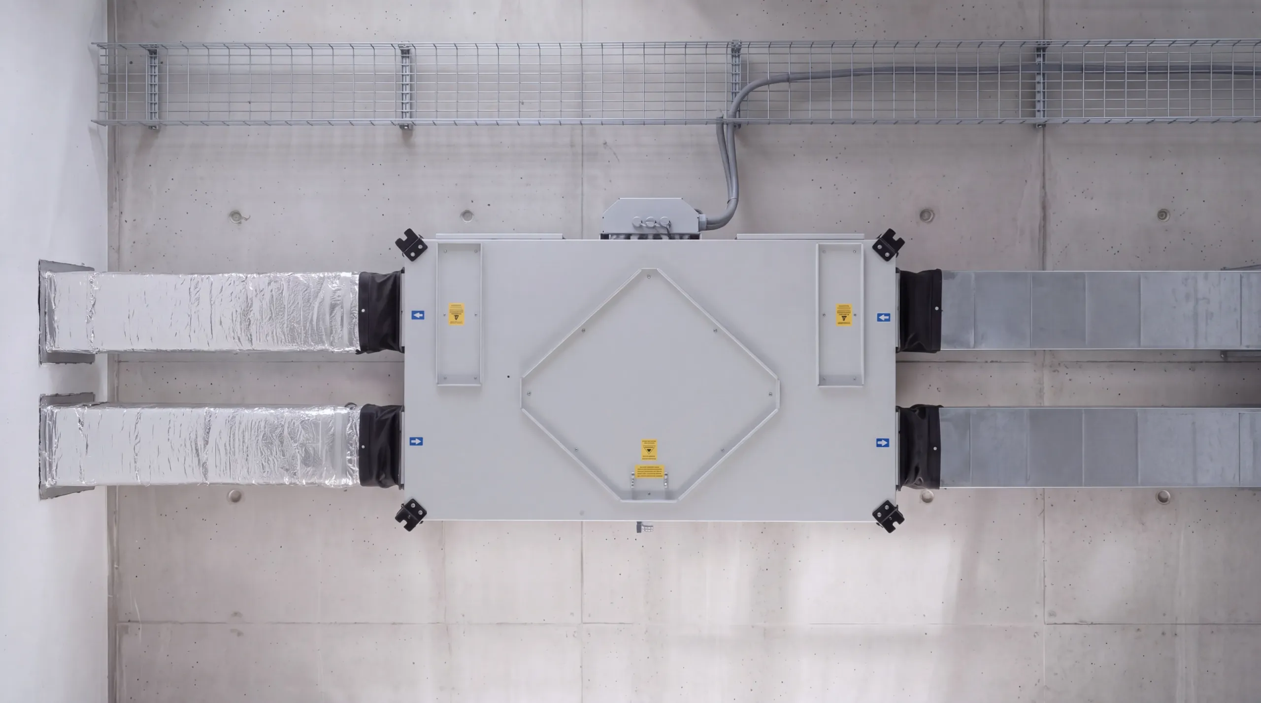 Alttan görünüm: beton döşemeye asılı Technogen Superair tavan tipi ısı geri kazanım cihazı ve dört ayrı dikdörtgen kanal bağlantısı; bir uçta taze hava ve egzoz, diğer uçta besleme ve dönüş